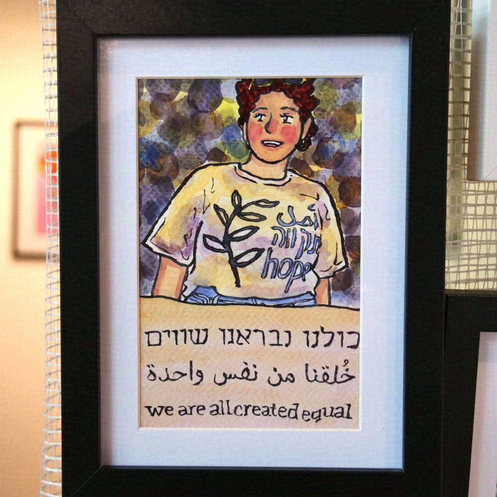 Vertical painting done with ink lines and watercolour paint. On the bottom third is a piece of cloth, slightly pinkish-yellowish saying "we are all created equal" in Hebrew, Arabic, English. Above is a young woman smiling and looking to the right, with curly hair and glasses in the hair, the shirt of hers, short sleeved, says "Hope" in Arabic, Hebrew, English, with an olive branch to the left. The dark background is painted in circles of different colours. The painting is signed Tel Aviv Jaffa Michael Vokabre 2024 5785. The painting is in black frame with white background in between the frame and the painting, behind is a plastic net on which the painting hangs.