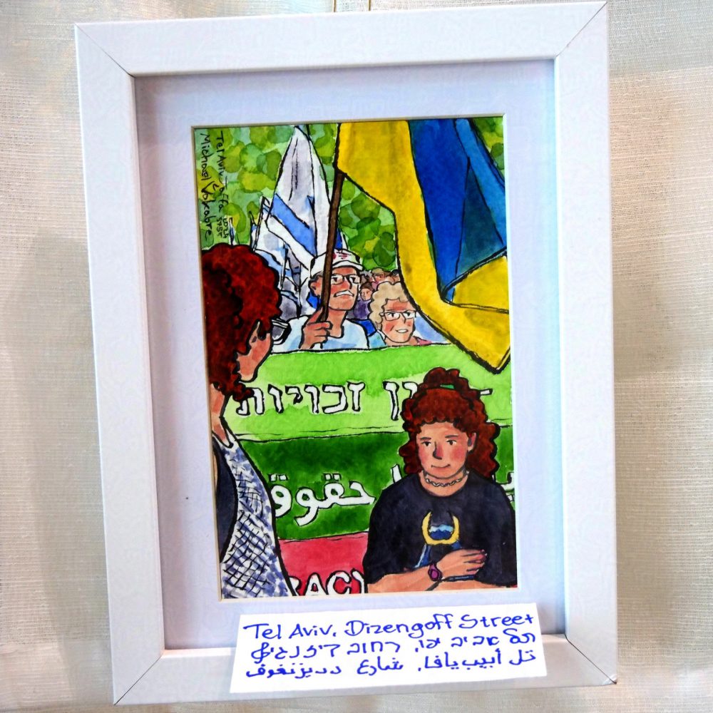 Vertical painting in watercolour with ink lines, a march in front of the green background painted in circles. In front is a young participating girl facing in front, and a woman looking back at the march. Part of the front banner can be seen, in Hebrew, Arabic, English, in light green, dark green and red. Behind is a man holding Ukrainian flag, and other people holding Israeli flags. The painting is in white frame with white background, on white cloth, with a piece of paper with it signed in English, Hebrew, Arabic below.