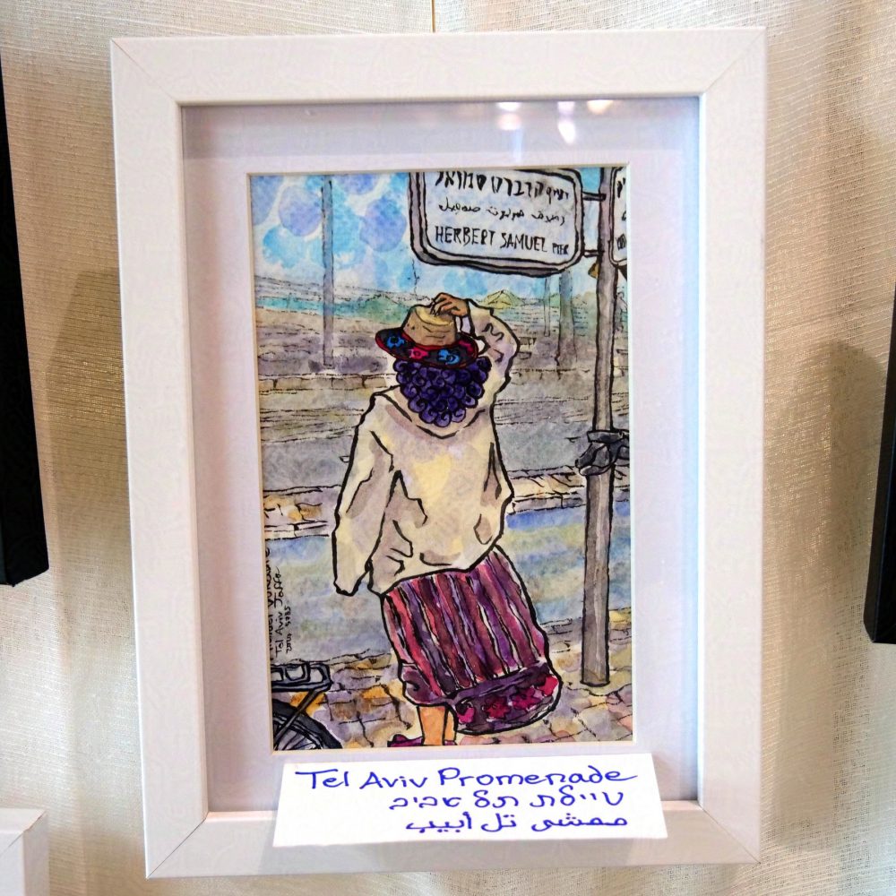 Vertical painting in watercolour with ink lines. In the middle stands, with the observer from the back, a woman with purple curly hair in a long white-yellowish shirt and dark red skirt, holding onto a hat with flower pattern. On the left peeks is a wheel of a bicycle, and on the right is a street sign on a pole saying "Herbert Samuel Pier" in Hebrew, Arabic, English. To the right of the address tied a street food cart. In the background is a two-lane road, and a pedestrian sidewalk with sea behind the fence of the sidewalk. The sky is painted in circles of different colours. The painting is in white frame on white background, handing off white cloth. It's signed by hand below in English, Hebrew, Arabic.