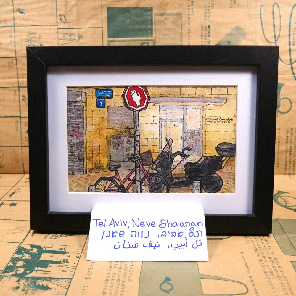 Horizontal painting of an evening street scene, in the back is a wall with a light up entrance to an apartment house, in front of the entrance is a parked motor scooter, and to the left of the scooter is a slightly bent bright "Stop" sign. The stop sign in Israel and Palestine is a white hand on octogonal red background with a white line on the corner. In front of the pole with the sign is a bicycle. Two bollards and a bush are peeking in front. In the back, left from the entrance to the apartment buildings is an electric box with graffiti and stickers on top, a ventilation grill, and on the left from it part of the shut entrance to a shop. Above is a street sign and a building sign saying "one". The painting is signed on the right as Michael Vokabre (in Latin) then in Hebrew Tel Aviv Jaffa, then in numbers 2024 5785. The painting is framed on white background in a black frame, below is a piece of paper saying "Tel Aviv, Neve Shaanan" in English, Hebrew, Arabic. The background is a catalogue of Gekko-so shop looking like a newspaper, yellow paper with green print.
