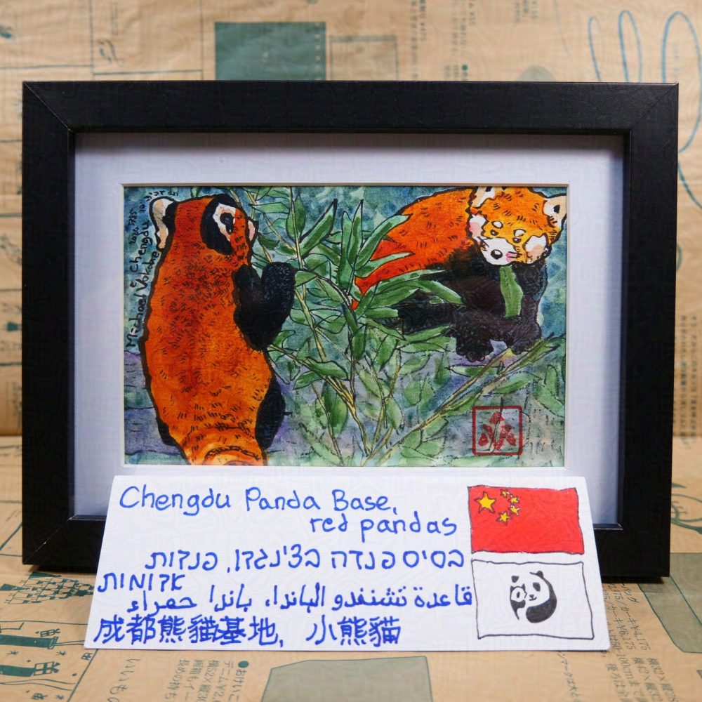 Horizontal painting, in ink with watercolour lines. On the left is a red panda holding a bamboo branch, to the back to the observer. On the right is another red panda on a stump chewing a bamboo leaf, part of the red panda obscured by the branch. Below is a plaque, hand-written, in English, Hebrew, Arabic and Chinese, with a flag of P.R.China and Chengdu Panda Base to the right. The painting is in a black frame with white background between the painting and the frame.  Behind is a newspaper-like catalogue of Gekko-so art shop in Tokyo.