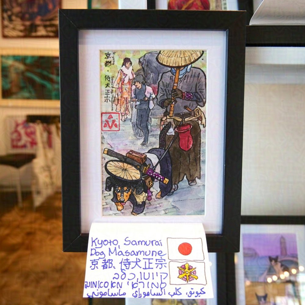 The painting described before is photographed framed affixed to the corner of a stall being sold at the port of Jaffa. In the background are other paintings, on the wall to the left, and one on the stall, with cats, to the right. The frame is black, and in between the frame and the painting is white background. Below the painting is a sheet of paper with hand-written description of the painting in English, Japanese, Arabic and Hebrew. To the right of the description is the flag of Japan and the flag of Kyoto City.