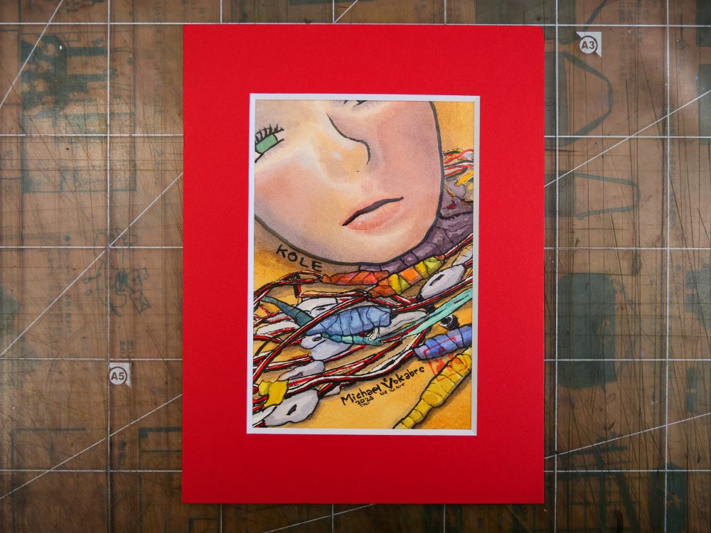 Vertical painting, in watercolour with ink lines. On top left is the part of the robot head covered in realistic silicone skin, lying on the table. The eyes are half-closed and are shiny green. Below the head are numerous cables, red-white-black with connectors covered in plastic and tape of different colours. The painting is in a red frame on a transparent cutting board with paper below it.